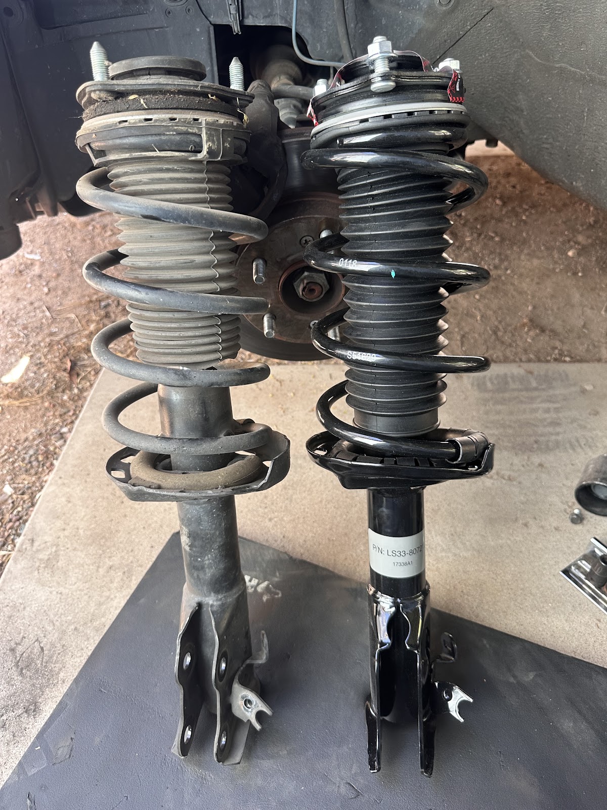 Worn strut assembly standing next to the new strut and spring, ready to be installed