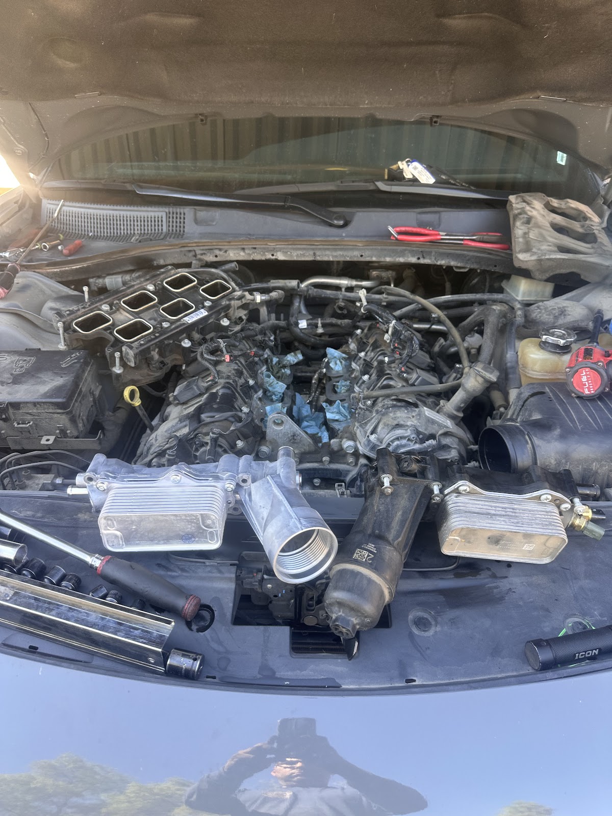 Engine bay opened up with the intake removed and old and new oil coolers laid across the cowl mid-repair