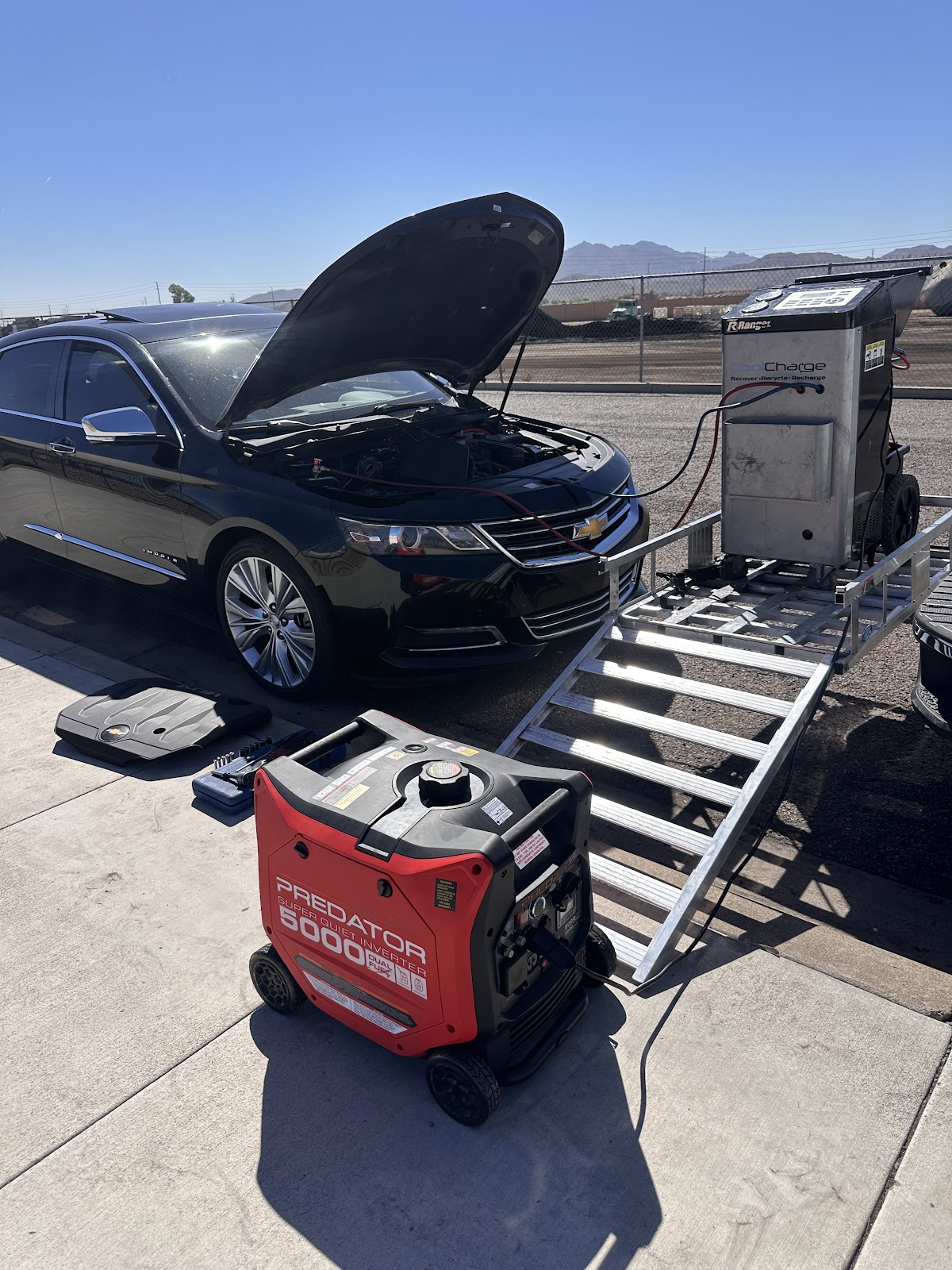Sedan with its hood up in a parking lot, Albert's generator and equipment ramped down from the trailer beside it