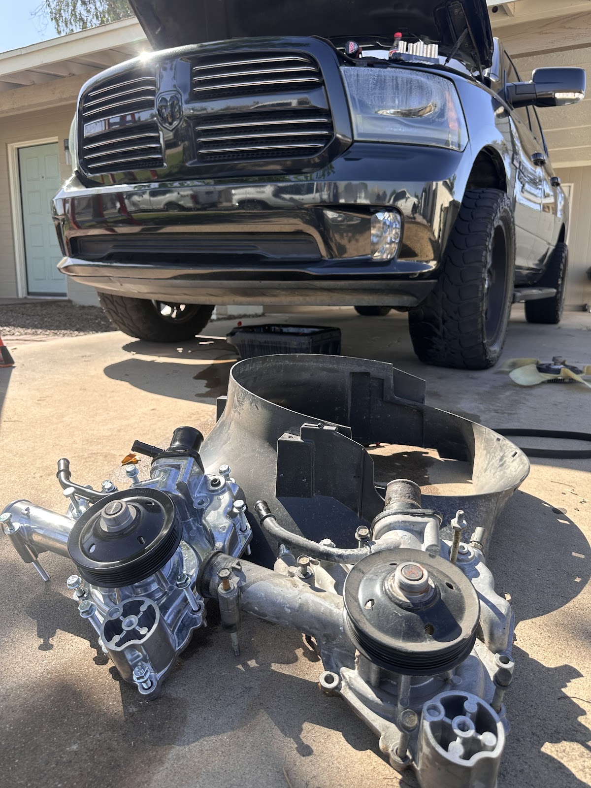 Old and new water pumps sitting side by side on the driveway in front of a pickup with its hood up