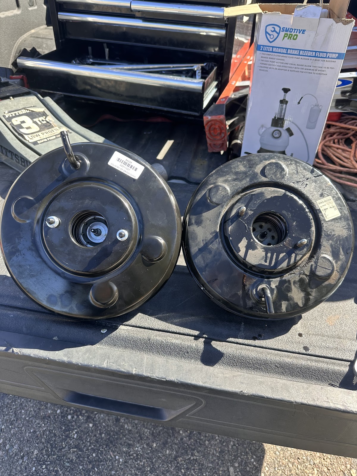 Two brake boosters, the worn one and its replacement, laid out on the truck bed next to the toolbox
